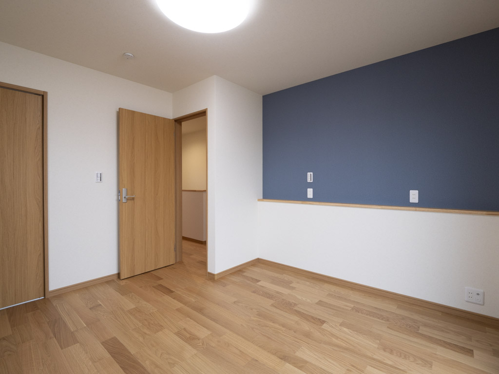 アクセントクロスに睡眠を妨げないブルー系のクロスを採用しました。 また、ベットの枕元に小さな棚を設け、コンセントを配置、スマホの 充電等に使い勝手の良い棚を作りました。